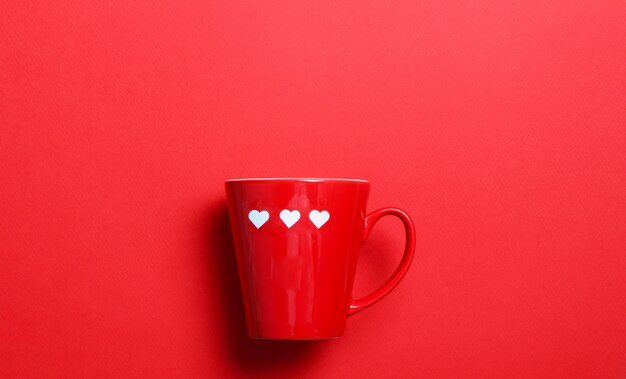 Tazza di caffè rossa con cuori bianchi sulla parete rossa