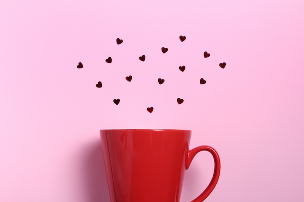 Tazza di caffè rossa con cuori glitter rosso sulla parete rosa. Composizione piatta. Romantico, concetto di San Valentino.