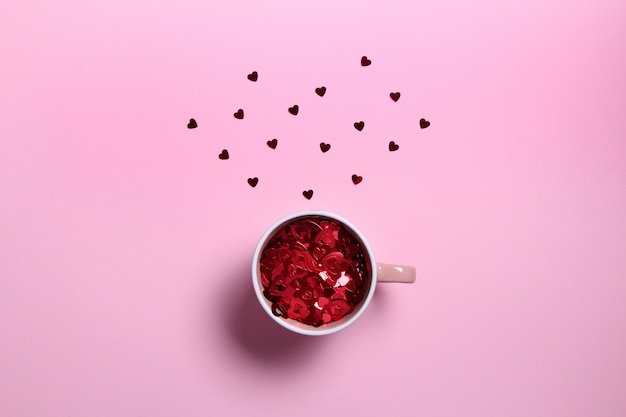 Tazza di caffè rossa con cuori glitter rosso sulla parete rosa. Composizione piatta. Romantico, concetto di San Valentino.