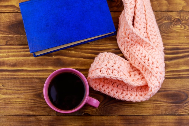 Tazza di caffè, sciarpa lavorata a maglia e libro su fondo di legno