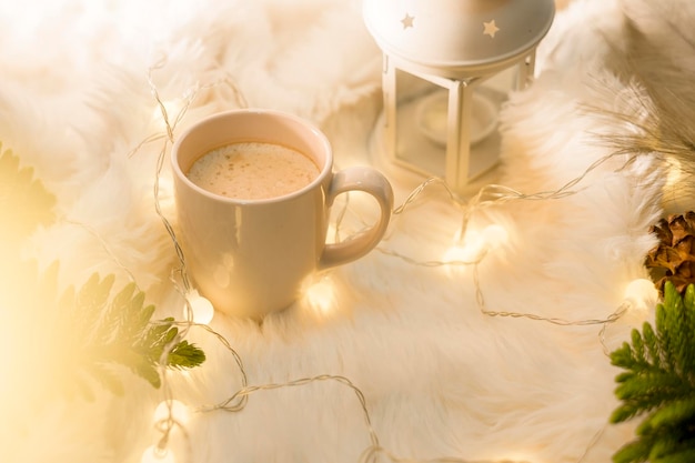 Tazza di caffè sopra il bokeh delle luci di Natale in casa sulle decorazioni della tavola di legno Vacanze invernali