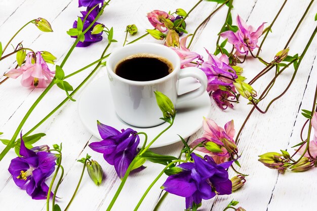 Tazza di caffè su un tavolo di legno bianco con fiori di aquilegia rosa e blu