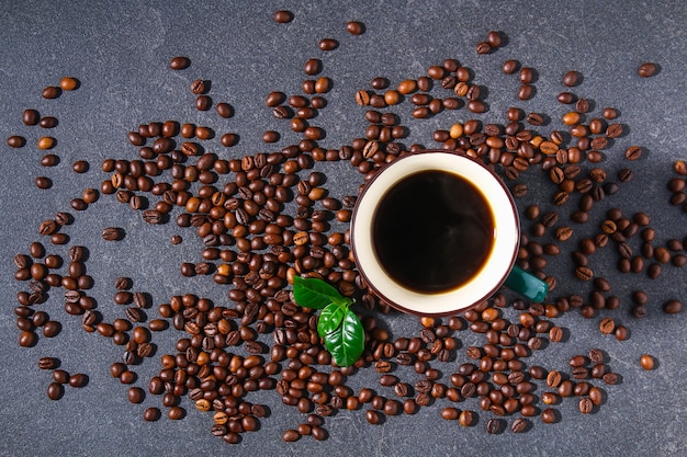 Tazza di caffè su un tavolo grigio con chicchi di caffè e foglie di caffè