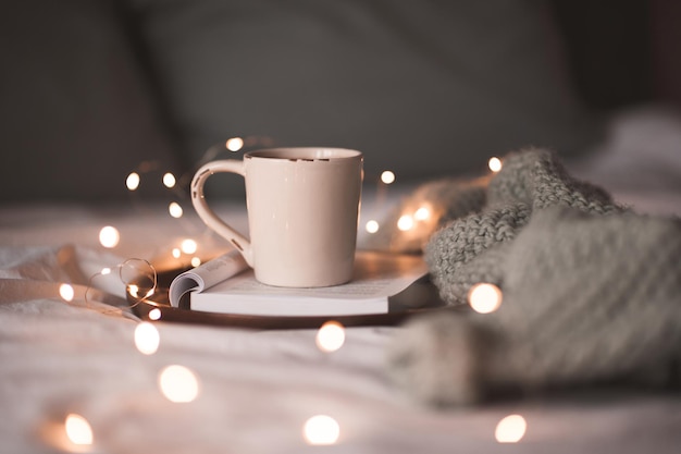 Tazza di caffè sul libro aperto con maglione lavorato a maglia a letto da vicino. Buon giorno. Stagione delle vacanze invernali.