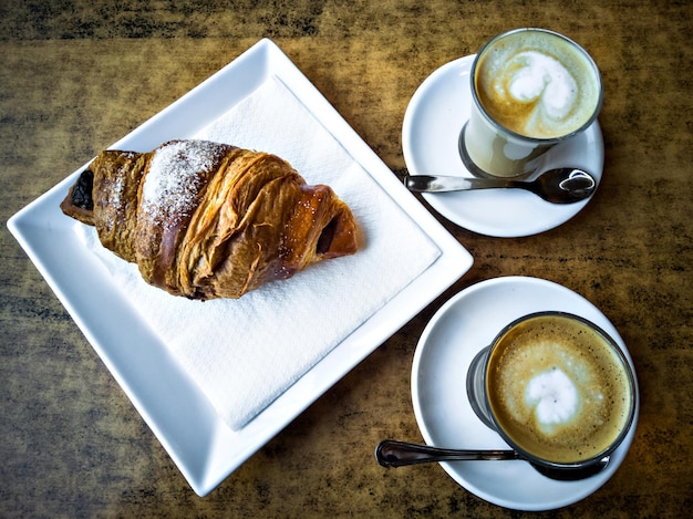 Tazza di caffè sul piatto e cucchiaio con croissant.