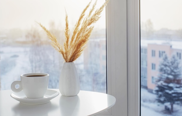 Tazza di caffè sul tavolo bianco vicino alla finestra in inverno