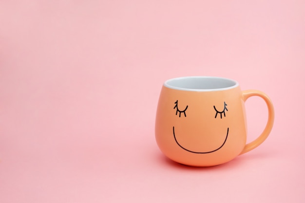 Tazza di caffè sulla parete rosa con la faccia di sorriso felice sulla tazza.