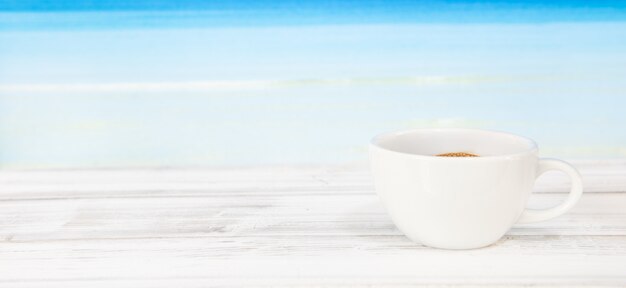Tazza di caffè sulla tavola di legno bianca con il mare blu luminoso