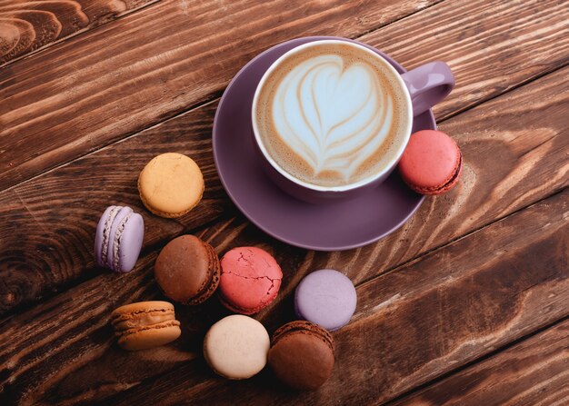 Tazza di caffè viola con cuore e amaretti colorati sullo sfondo in legno vista dall'alto