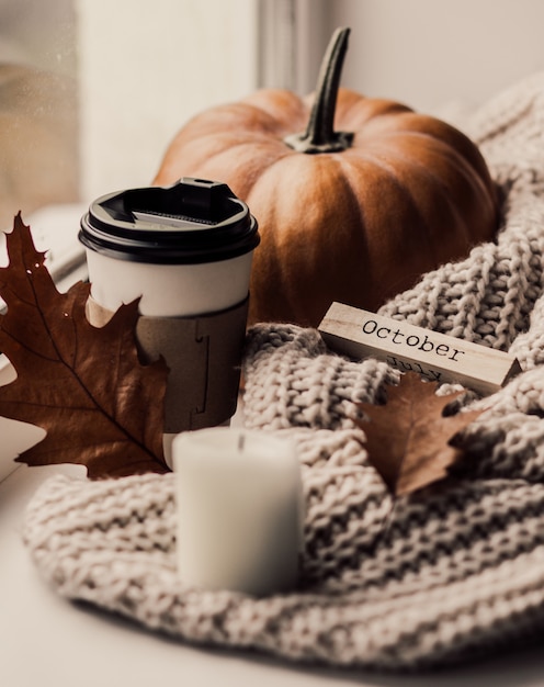 Tazza di caffè, zucca, foglie di autunno secche sulla finestra.