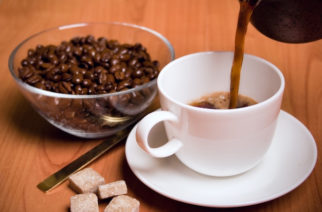 Tazza di caffè, zucchero e fagioli in ciotola di vetro sul tavolo di legno