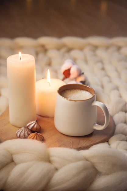 Tazza di cappuccino, biscotti e candele sullo sfondo di una coperta di filato spesso. L'atmosfera di familiarità e comfort.