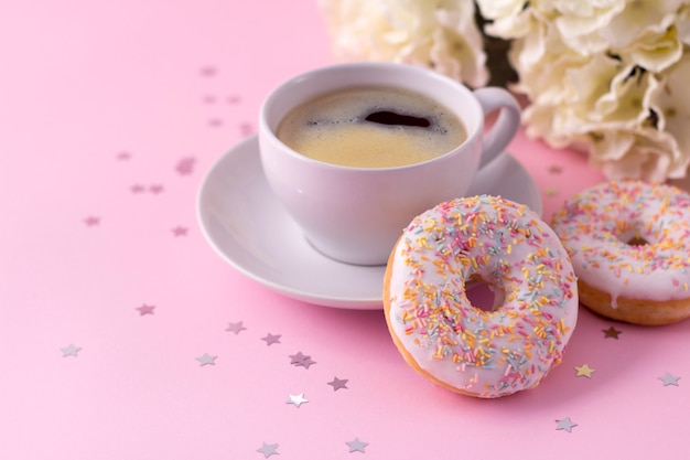 Tazza di cappuccino caldo e due ciambelle con fiori rosa