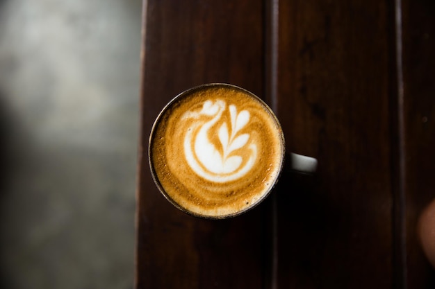 Tazza di cappuccino caldo sullo scrittorio di legno sul fondo scuro della tavola