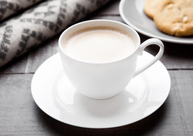 Tazza di cappuccino con sciarpa di lana grigia e biscotti su superficie di legno