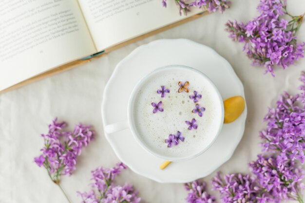 Tazza di cappuccino su una superficie beige. Fiori lilla, libro.