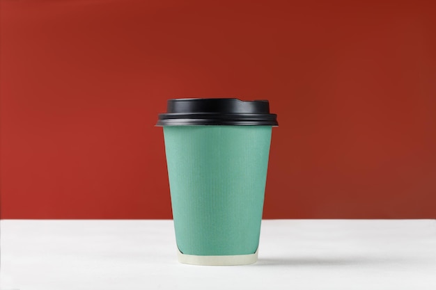 Tazza di carta verde con caffè su sfondo bianco e parete rossa Mockup di primo piano della tazza di carta usa e getta