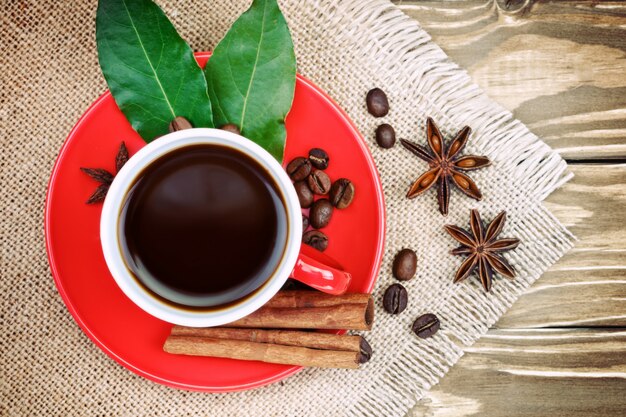 Tazza di ceramica rossa con supporto per caffè su assi di legno e tela con chicchi di caffè sparsi
