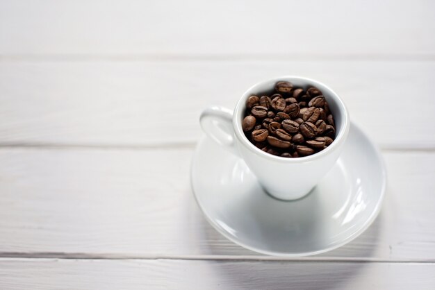 Tazza di chicchi di caffè aromatici su un fondo di legno bianco