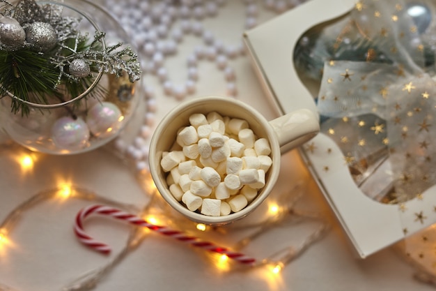 Tazza di cioccolato con marshmallow, decorazioni natalizie su tavolo bianco, bastoncino di zucchero e confezione regalo