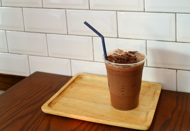 Tazza di cioccolato ghiacciato condita con un pezzo di cioccolato sul vassoio in legno pronto per il takeaway