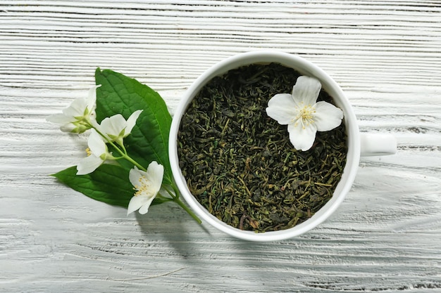 Tazza di foglie di tè verde e fiori di gelsomino su sfondo di legno