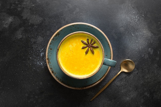 Tazza di latte ayurvedico dorato di latte di curcuma con polvere di curcuma e anice stellato sul nero. Vista dall'alto