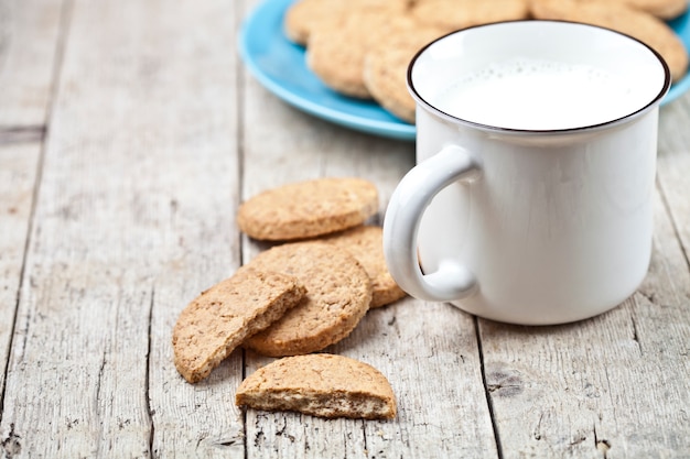 Tazza di latte e biscotti di avena al forno freschi sul piatto ceramico blu sulla tavola di legno rustica