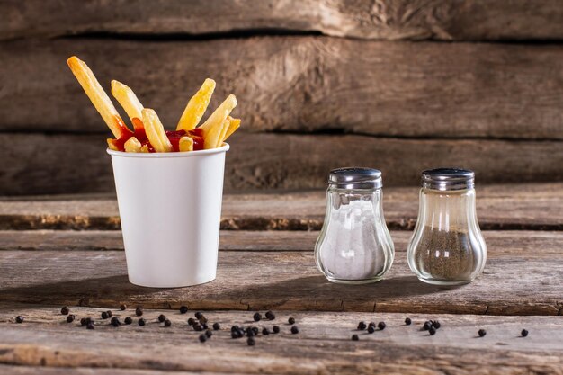 Tazza di patatine fritte con pepperbox Sale pepperbox e patatine Fast food snack sul tavolo Così fresco e croccante