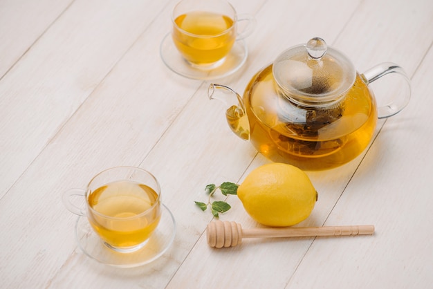 Tazza di tè al limone con miele su fondo di legno bianco.