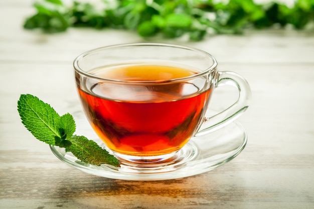 Tazza di tè alla menta sulla tavola di legno delle foglie.