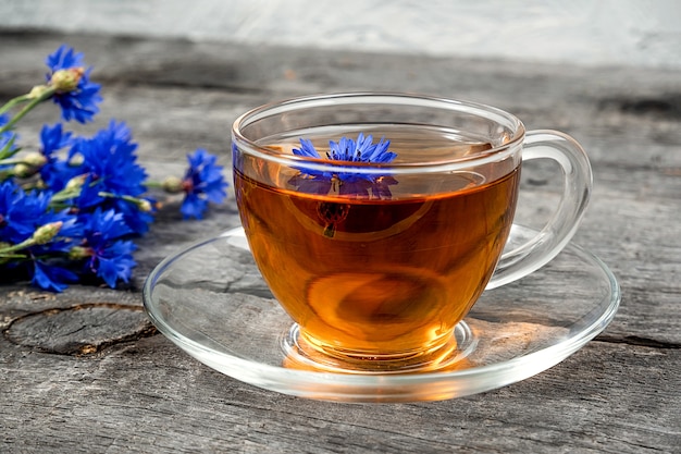 Tazza di tè alle erbe e fiori di fiordaliso blu sulla superficie del legno