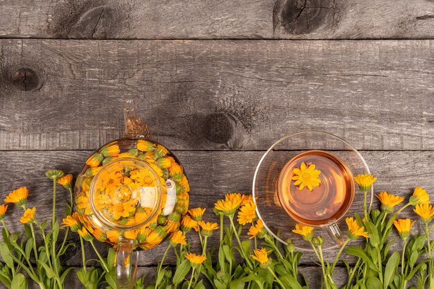 Tazza di tè alle erbe e teiera trasparente e fiori di calendula su legno