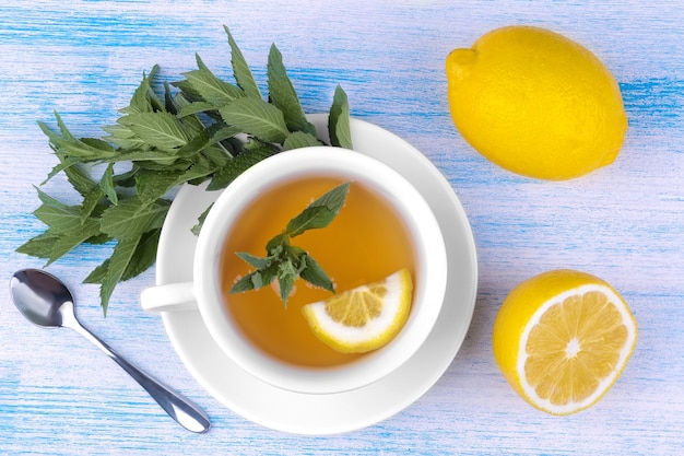 Tazza di tè bianca con menta e limone su uno sfondo di legno blu vista dall'alto