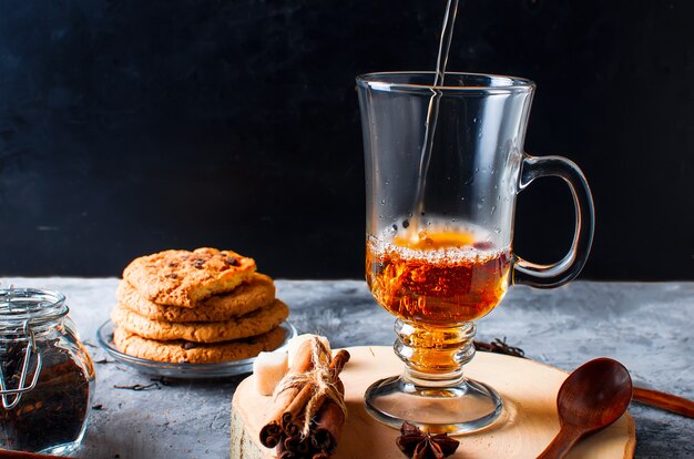 Tazza di tè, biscotti, cannella, anice su sfondo scuro