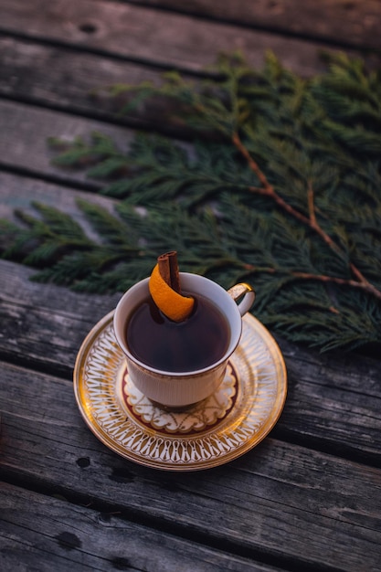 Tazza di tè calda, arancione, cannella, verdura sulla tavola di legno, sera.