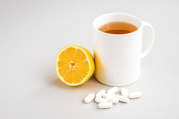 Tazza di tè caldo con limone e pillole su una superficie di legno. Malattia catarrale. Stagione influenzale.