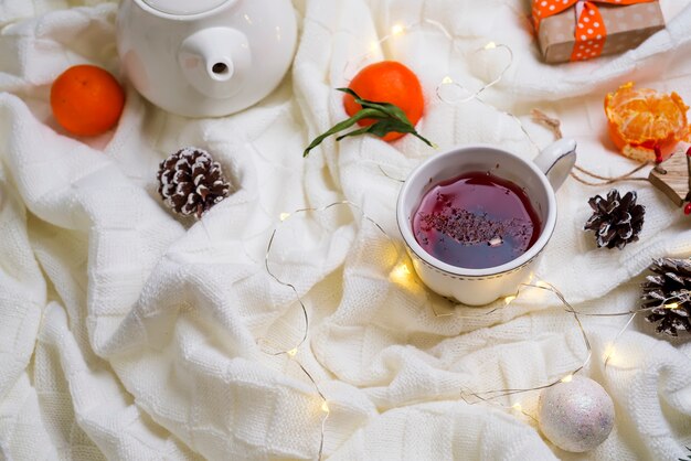 Tazza di tè caldo con mandarini e maglioni sul letto