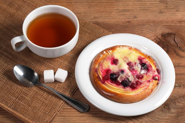 Tazza di tè caldo e panino con marmellata e crema pasticcera sul vecchio tavolo di legno