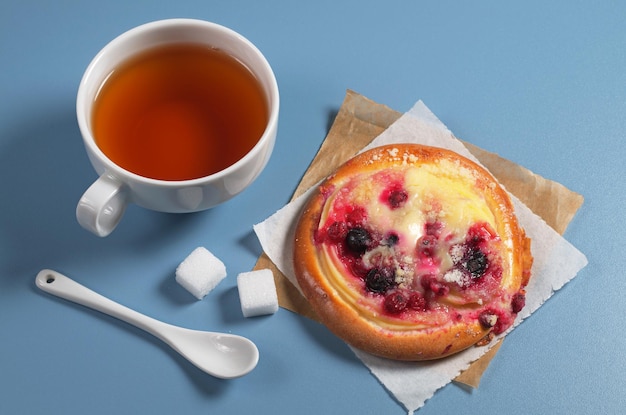 Tazza di tè caldo e panino dolce con marmellata e crema pasticcera sul tavolo blu