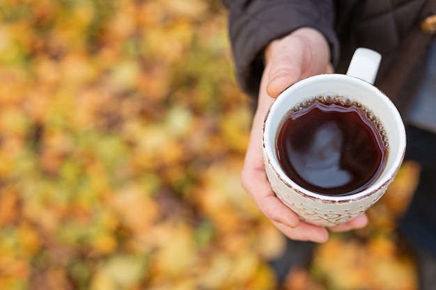 Tazza di tè caldo nero in mano all'aperto. Passeggiata nella foresta autunnale Copia spazio - Immagine