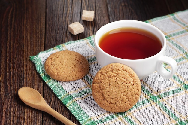 Tazza di tè con biscotto di farina d'avena su tavolo in legno scuro tovaglia verde nascosta