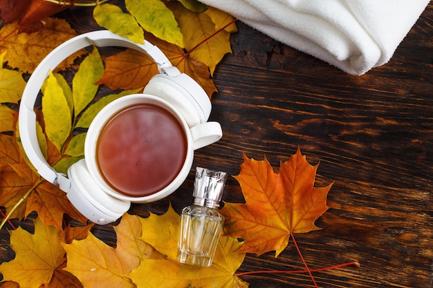 Tazza di tè con foglie di autunno plaid bottiglia di profumo e cuffie su sfondo di legno