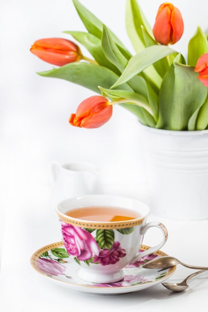 Tazza di tè con i tulipani rossi sopra bianco