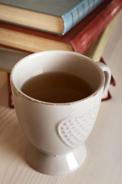 Tazza di tè con la pila di libri sulla tavola di legno sulla priorità bassa chiara della parete