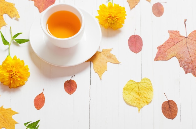 Tazza di tè con le foglie di autunno su fondo di legno