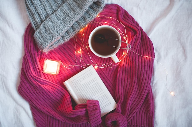 Tazza di tè con libro aperto e maglione lavorato a maglia in primo piano del letto. Vista dall'alto. Buon giorno.