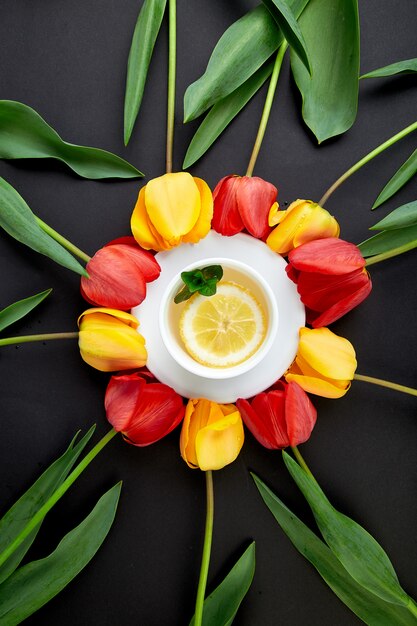 Tazza di tè con tulipano rosso e giallo intorno.