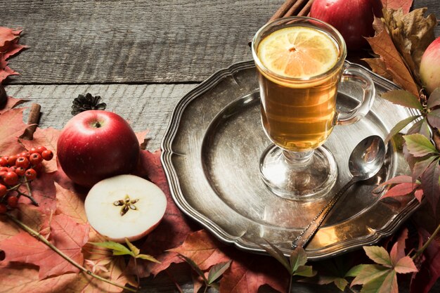 Tazza di tè di riscaldamento con la decorazione delle foglie e delle zucche di autunno sul bordo di legno. Cadere ancora vita.