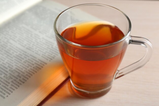 Tazza di tè di vetro con il libro aperto sul primo piano di legno della tavola